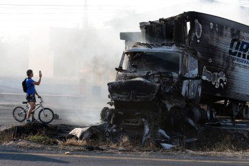 Ciclista fotografa caminhão incendiado por criminosos ligados ao Cartel de Jalisco Nueva Generación, perto Acatlan de Juarez, no estado de Jalisco - (crédito: Ulises Ruiz/AFP) Ciclista fotografa caminhão incendiado por criminosos ligados ao Cartel de Jalisco Nueva Generación, perto Acatlan de Juarez, no estado de Jalisco - (crédito: Ulises Ruiz/AFP)