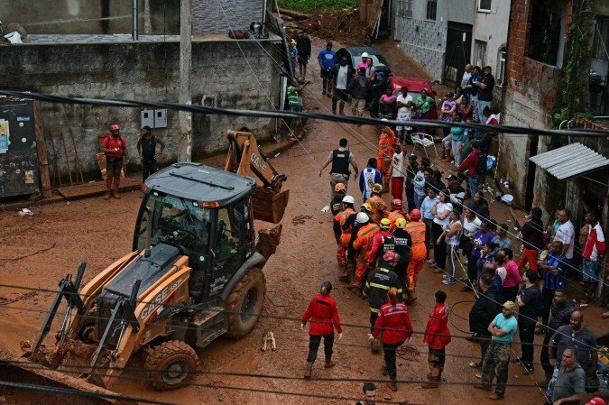 Equipes de resgate carregam um cadáver recuperado dos escombros, passando por uma retroescavadeira, após um deslizamento de terra causado por fortes chuvas no bairro Parque Jardim Burnier, em Juiz de Fora, Minas Gerais, Brasil, em 24 de fevereiro de 2026 - (crédito: PABLO PORCIUNCULA / AFP) Equipes de resgate carregam um cadáver recuperado dos escombros, passando por uma retroescavadeira, após um deslizamento de terra causado por fortes chuvas no bairro Parque Jardim Burnier, em Juiz de Fora, Minas Gerais, Brasil, em 24 de fevereiro de 2026 - (crédito: PABLO PORCIUNCULA / AFP)