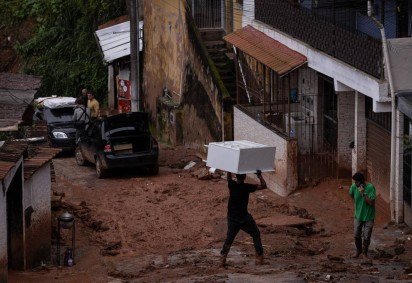 Morador carrega móvel na cabeça em rua enlameada de Juiz de Fora (MG), cidade atormentada pelas chuvas fortes há dias -  (crédito: Eduardo Anizelli/Folhapress)