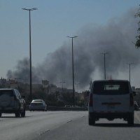 Motoristas dirigem por uma rua enquanto a fuma&ccedil;a sobe ap&oacute;s um relato de ataque iraniano na &aacute;rea onde est&aacute; localizada a Embaixada dos EUA, na Cidade do Kuwait -  (crédito:  AFP)