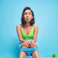  Thoughtful unhappy Asian woman sits on toilet bowl looks displeased aside keeps hands on knees poses in restoom pees or defecates reveals herself surrounded by hygiene products isolated over blue wall
     -  (crédito: Reprodu&ccedil;&atilde;o Freepik)