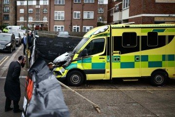 Um membro (à esquerda) da comunidade judaica observa a cena de um ataque incendiário antissemita através de uma cerca improvisada no bairro de Golders Green, no norte de Londres, em 24 de março de 2026       -  (crédito: HENRY NICHOLLS / AFP)