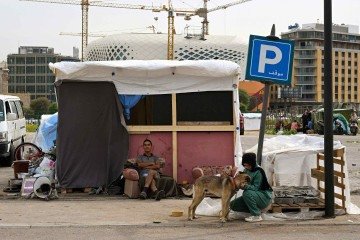 Uma menina acaricia seu cachorro do lado de fora de sua barraca em um acampamento não oficial para pessoas em situação de rua na área portuária de Beirute, em 14 de abril de 2026       -  (crédito: JOSEPH EID / AFP)