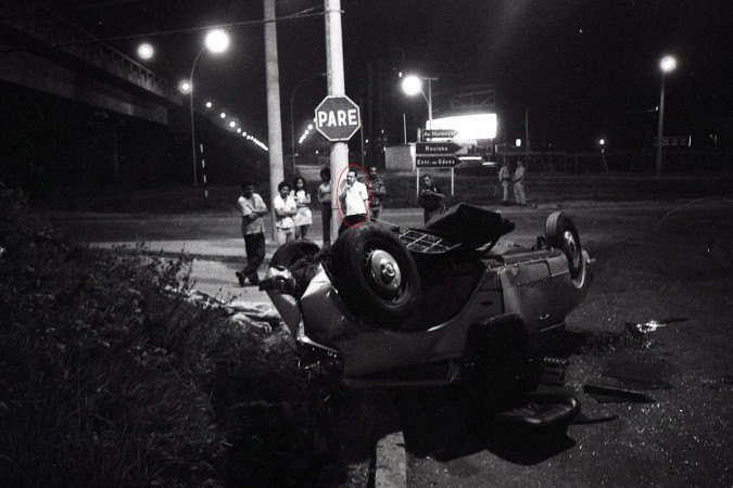 Rio de Janeiro (RJ) - 14/04/1976 - Na foto, preta-e-branca, Perdigão aparece encostado em um poste, com uma camisa clara, levando a mão direita ao rosto, olhando para o carro da vítima. 
