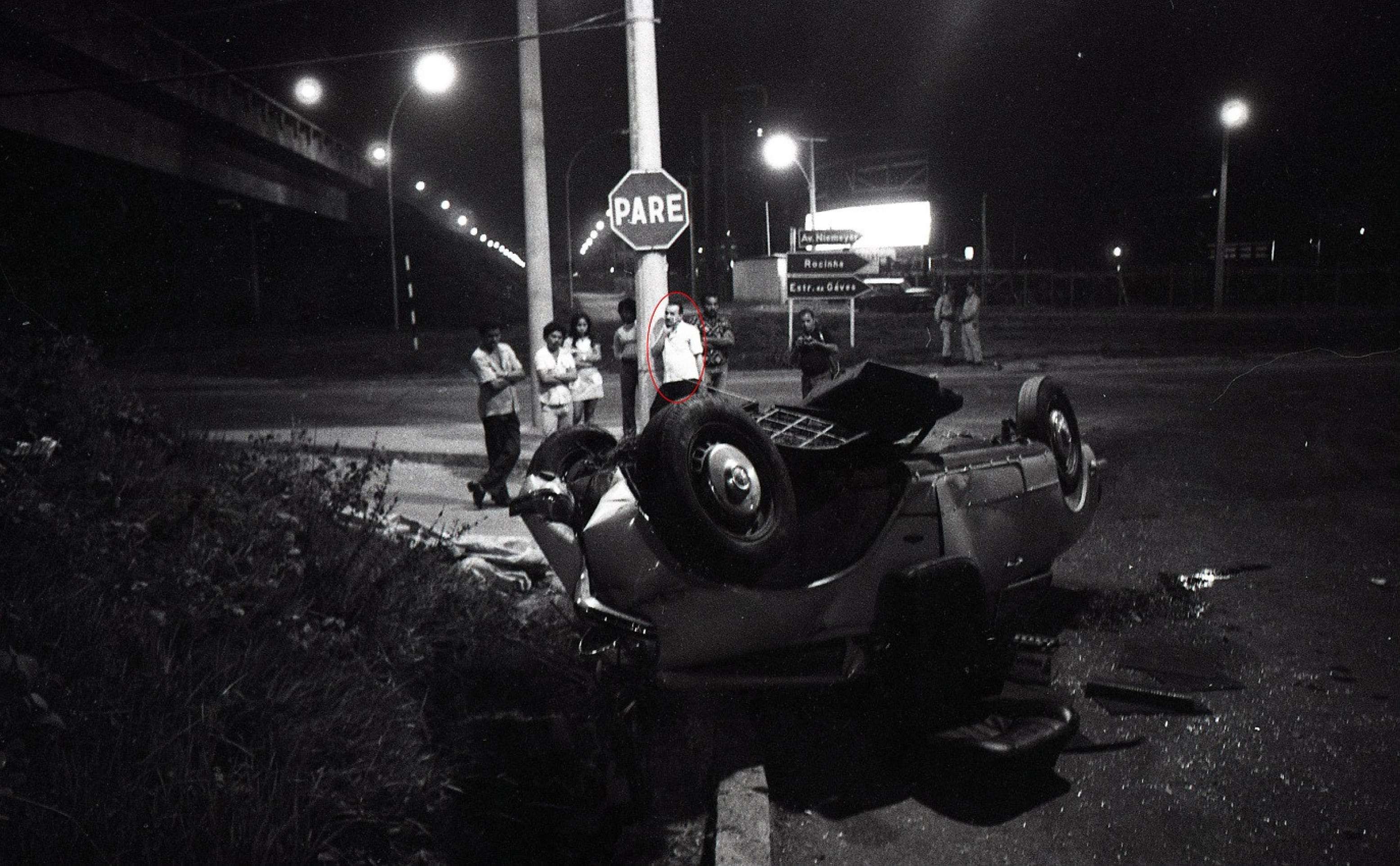 Rio de Janeiro (RJ) - 14/04/1976 - Na foto, preta-e-branca, Perdig&atilde;o aparece encostado em um poste, com uma camisa clara, levando a m&atilde;o direita ao rosto, olhando para o carro da v&iacute;tima. 