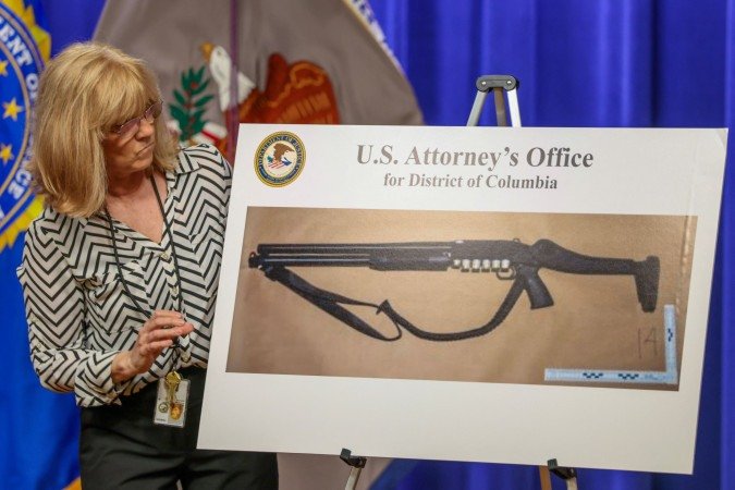 Funcionária do Departamento de Justiça mostra espingarda usada