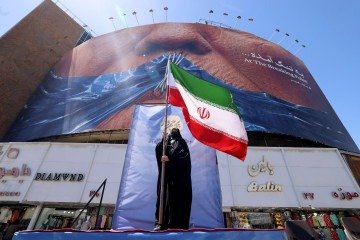 Uma mulher segura a bandeira iraniana enquanto está em frente a um outdoor anti-EUA que faz referência ao presidente Donald Trump e ao Estreito de Ormuz, instalado em um prédio na Praça Valiasr, em Teerã, em 10 de maio de 2026 -  (crédito: ATTA KENARE / AFP)