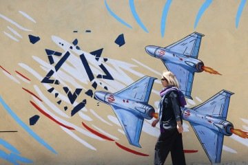 Uma mulher iraniana passa por um mural anti-EUA e anti-Israel pintado em uma parede na capital Teerã, em 10 de maio de 2026 -  (crédito: ATTA KENARE / AFP)