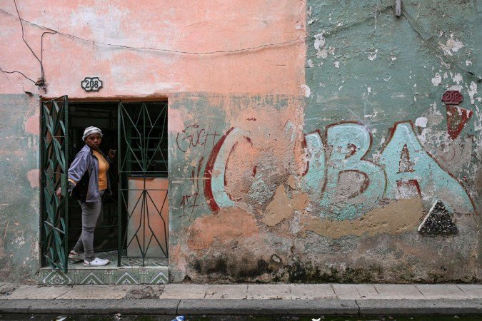 Moradora olha da porta de casa ao lado de um muro com a palavra Moradora olha da porta de casa ao lado de um muro com a palavra