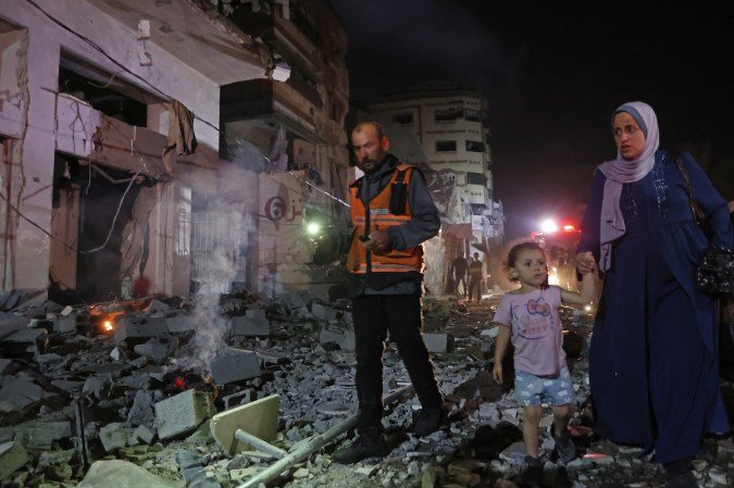 Primeiro socorrista escolta mulher e criança entre escombros, em Rimal, bairro da Cidade de Gaza 