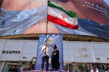 Iraniano agita a bandeira da República Islâmica em praça de Teerã, diante de outdoor que ironiza o presidente norte-americano -  (crédito: Atta Kenare/AFP)
