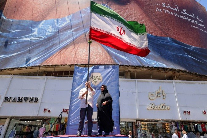 Um homem hasteia a bandeira nacional iraniana enquanto está em um pódio diante de um cartaz político com o presidente dos EUA, Donald Trump, e o Estreito de Ormuz, na Praça Valiasr, em Teerã, em 26 de maio de 2026 - (crédito: ATTA KENARE / AFP) Um homem hasteia a bandeira nacional iraniana enquanto está em um pódio diante de um cartaz político com o presidente dos EUA, Donald Trump, e o Estreito de Ormuz, na Praça Valiasr, em Teerã, em 26 de maio de 2026 - (crédito: ATTA KENARE / AFP)
