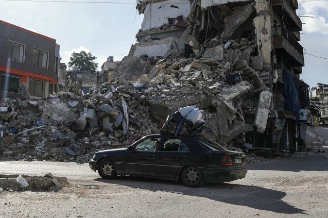 Carro de refugiados passa diante de prédio destruído durante bombardeios israelenses, na cidade de Nabatieh, no sul do território libanês
