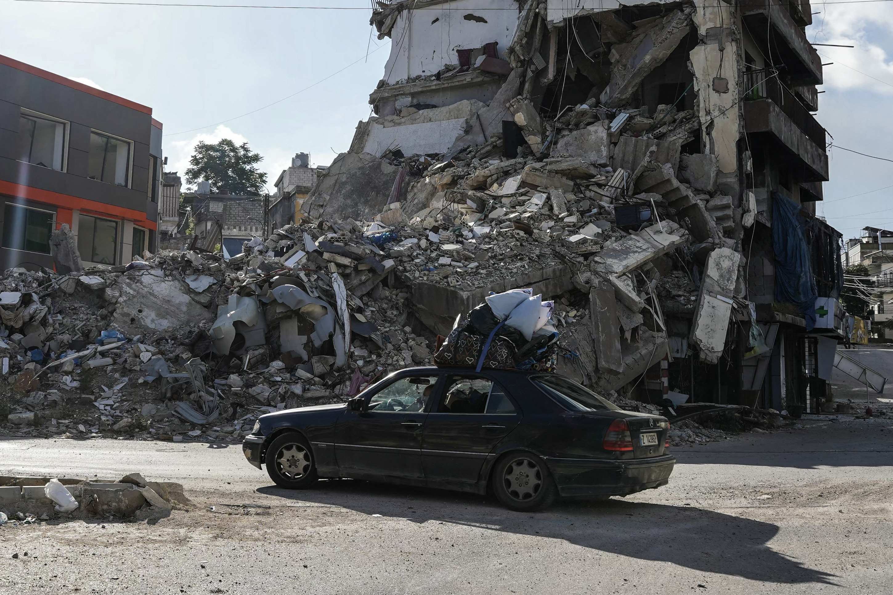 Carro de refugiados passa diante de pr&eacute;dio destru&iacute;do em bombardeios, na cidade de Nabatieh, no sul do L&iacute;bano 