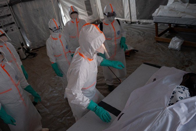 A team of doctors wearing protective suits works in a red zone inside the morgue, attend to the body of a man who died from Ebola virus disease as they allow the family see him for a last moment before its transfer to the cemetery in Bunia, Ituri Province, Democratic Republic of the Congo, on June 13, 2026. (Photo by Jospin Mwisha / AFP)
- (crédito: AFP) A team of doctors wearing protective suits works in a red zone inside the morgue, attend to the body of a man who died from Ebola virus disease as they allow the family see him for a last moment before its transfer to the cemetery in Bunia, Ituri Province, Democratic Republic of the Congo, on June 13, 2026. (Photo by Jospin Mwisha / AFP)
- (crédito: AFP)