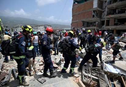  Members of search and rescue teams carry equipment across the rubble of damaged buildings in Catia La Mar, La Guaira, Venezuela, on June 26, 2026, following deadly earthquakes. The death toll from two powerful earthquakes that devastated Venezuela earlier this week rose to 920 on June 26, National Assembly President Jorge Rodriguez said. (Photo by Federico PARRA / AFP)
       -  (crédito:  AFP)