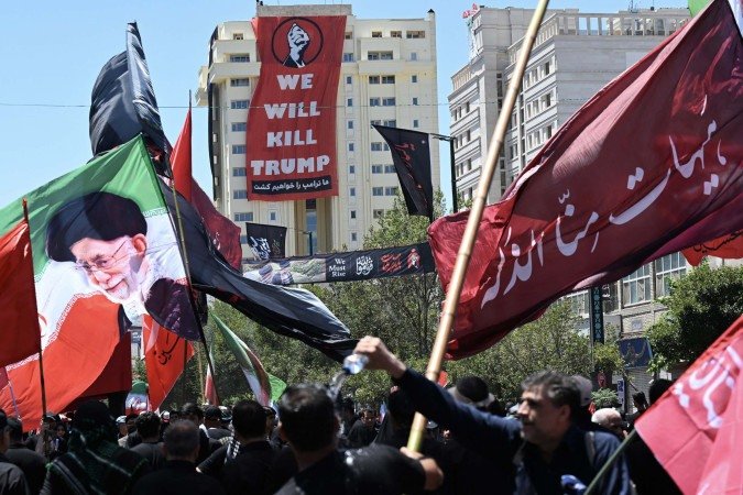Faixa estendida sobre prédio de Mashhad, durante funeral de Ali Khamenei, traz ameaça a Washington: - (crédito: Wakil Kohsar/AFP) Faixa estendida sobre prédio de Mashhad, durante funeral de Ali Khamenei, traz ameaça a Washington: - (crédito: Wakil Kohsar/AFP)
