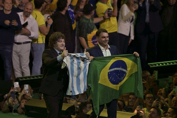  Argentina's President Javier Milei holds a national football jersey next to Brazil's right-wing presidential hopeful Flavio Bolsonaro holding a national flag during the launching of the latter's candidacy within the Liberal Party convention, in Sao Paulo, Brazil on July 25, 2026. Battered by a string of political crises, Flavio Bolsonaro launched his candidacy for Brazil's October presidential election, seeking to follow in the footsteps of his father, Jair Bolsonaro, who is serving house arrest for plotting a coup after losing the election in 2022. (Photo by Nelson ALMEIDA / AFP)
      