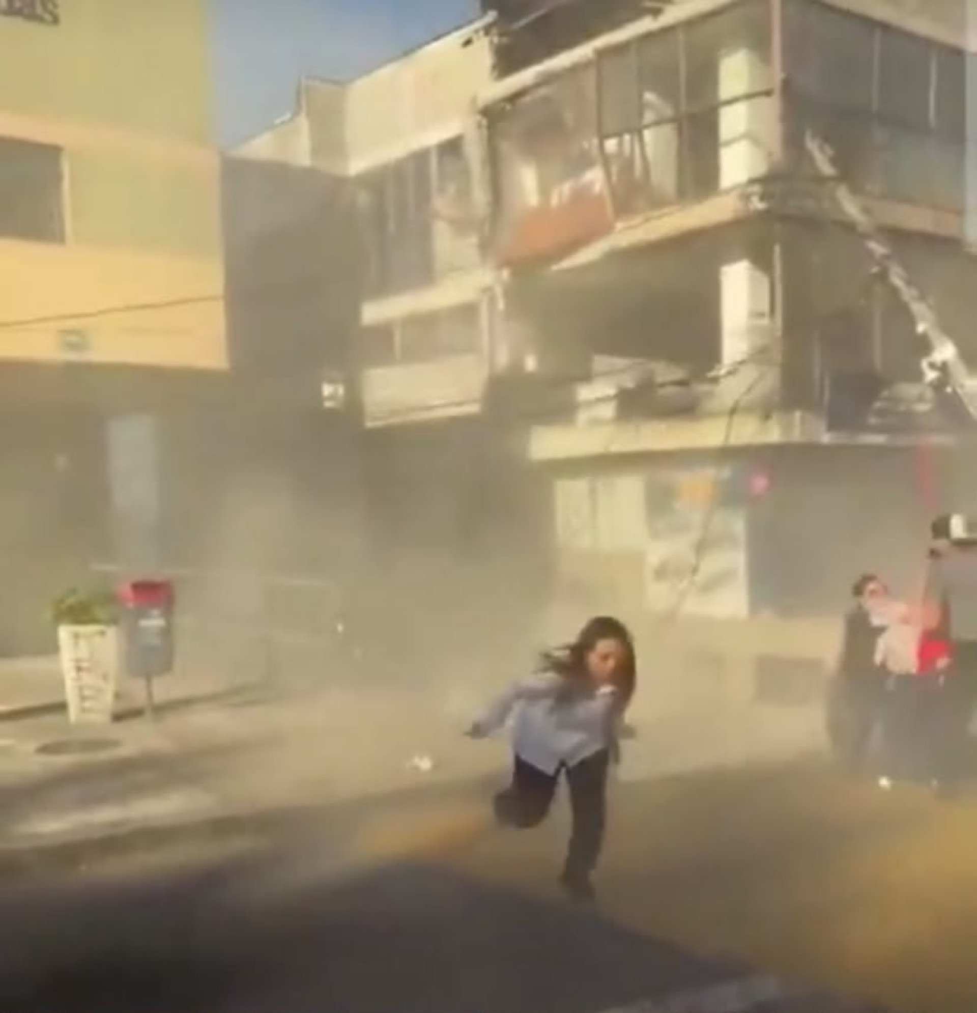 Mulher corre na tentiva de se proteger dos destroços caindo dos prédios, em Cali 