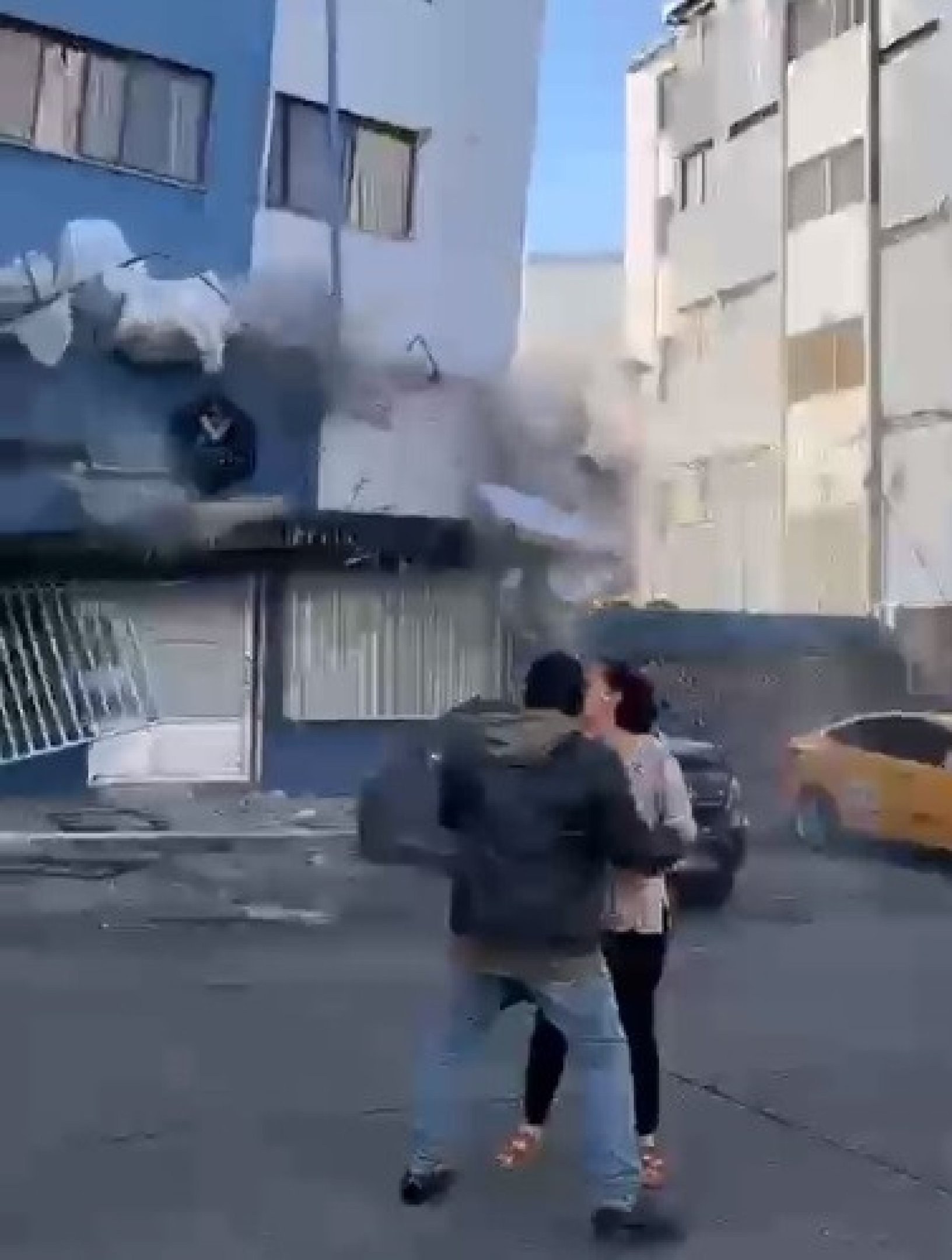 Casal se abraça em meio à rua, enquanto edifício cai, em Pereira 