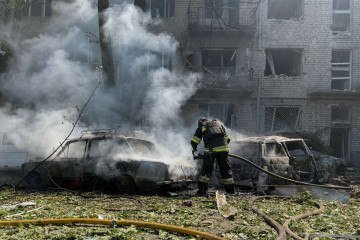 Um bombeiro ucraniano apaga o fogo em um carro próximo a um prédio residencial danificado no local de um ataque aéreo russo em Zaporizhzhia -  (crédito:  Darya Nazarova/AFP)