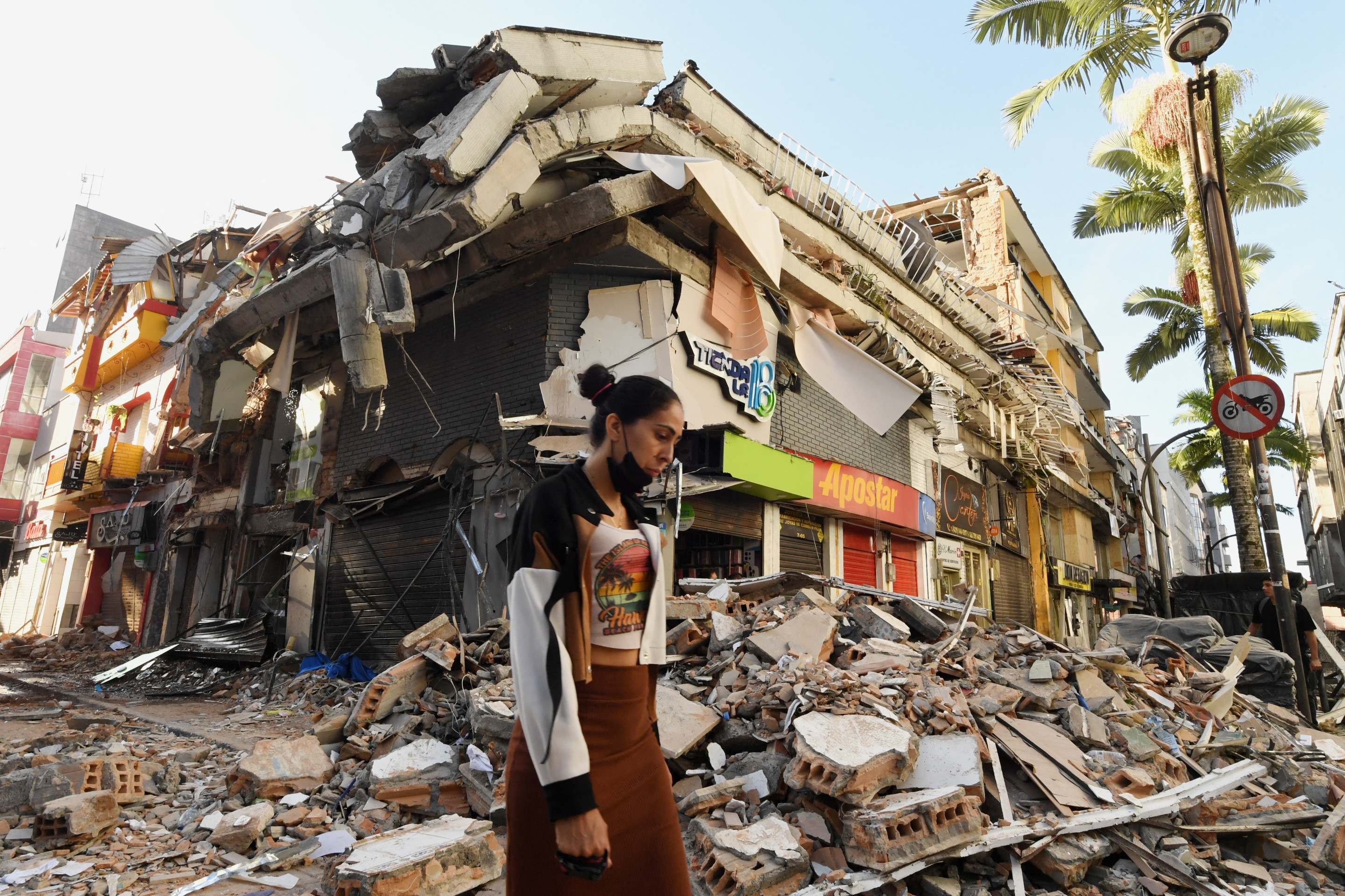 Mulher caminha diante de edif&iacute;cio em ru&iacute;nas, na mesma cidade: destrui&ccedil;&atilde;o generalizada 