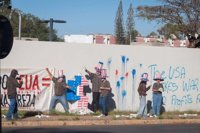 O episódio ocorreu por volta das 8h, quando um grupo pichou o muro do complexo diplomático com frases em português e inglês e ateou fogo a uma bandeira do país norte-americano - (crédito: Foto: Reprodução/Redes Sociais) O episódio ocorreu por volta das 8h, quando um grupo pichou o muro do complexo diplomático com frases em português e inglês e ateou fogo a uma bandeira do país norte-americano - (crédito: Foto: Reprodução/Redes Sociais)