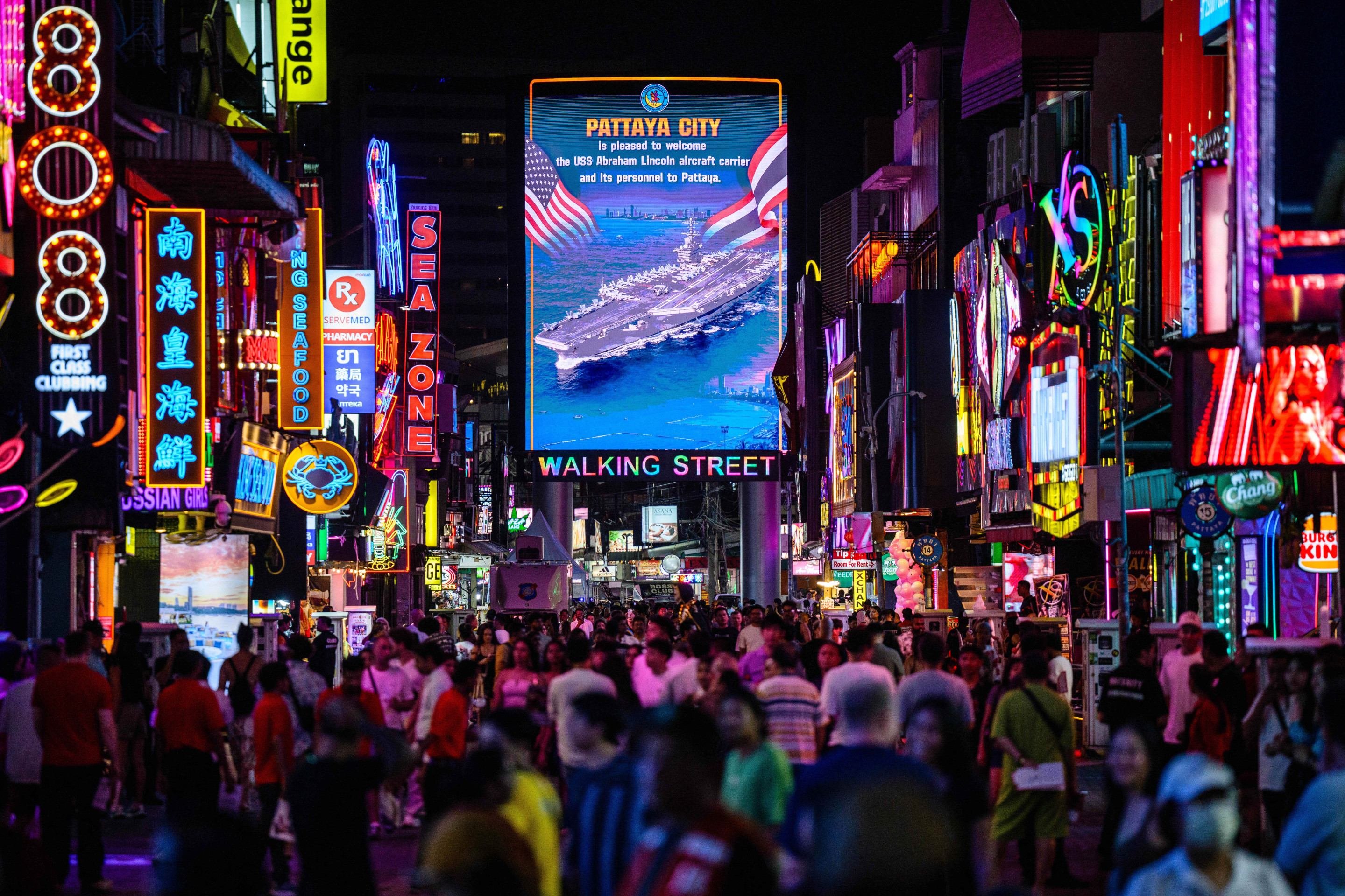 Pedestres caminham diante de imenso painel de LED com boas vindas aos marinheiros 