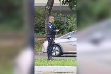  Policial aparece utilizando o celular enquanto observa os veiculos que passam pelo local -  (crédito:  Reprodução)