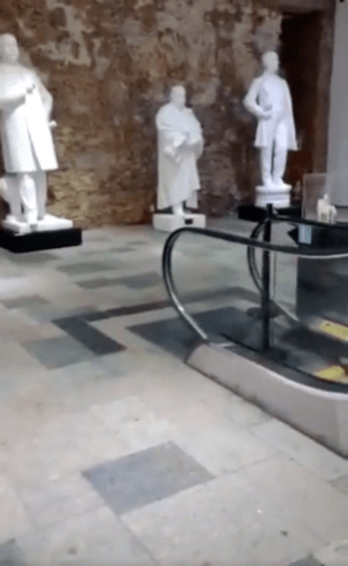 Capturas de tela dos segundos iniciais do v&iacute;deo investigado pelo Comprova que mostram as est&aacute;tuas, a escada rolante e, logo depois, a placa com a tarja preta no nome do ex-presidente Lula