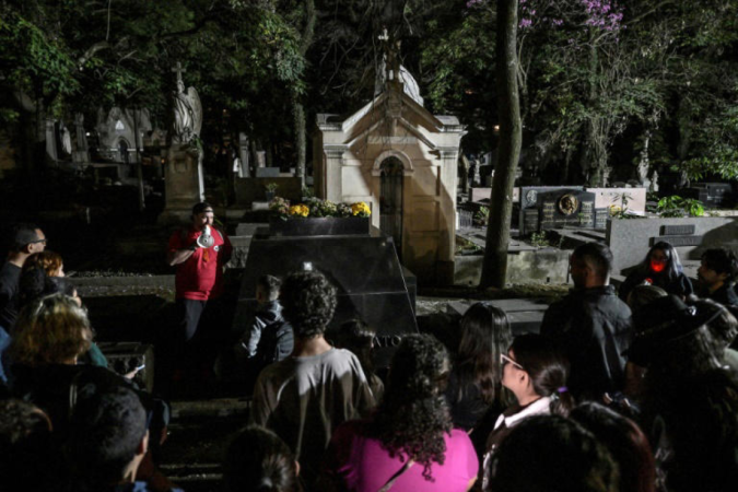 Visitantes ouvem o advogado Thiago de Souza (centro, em vermelho) durante visita noturna ao cemitério da Consolação, em São Paulo -  (crédito: AFP / Nelson Almeida)