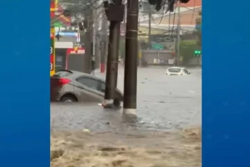 A mulher de 60 anos agarrada em um poste antes de ser arrastada pela enxurrada durante o temporal -  (crédito:  Reprodução / TV Band)